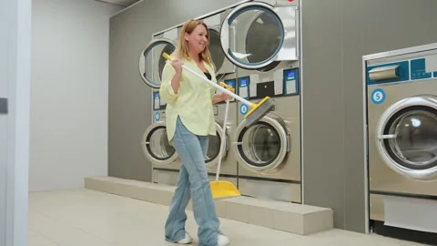 Happy Laundry Owner Dancing With Broom Dustpan Beside Industrial Washers 스톡 동영상 318848103