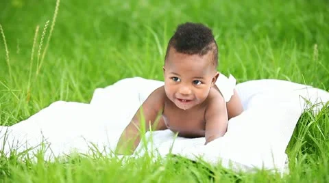 Happy little African American baby smiling while lying on blanket in garden. Stock Footage