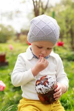 Happy little boy eats Easter Cake, in spring garden, outside. Cute happy litt Stock Photos