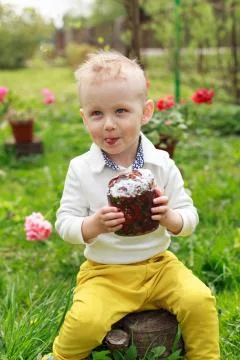 Happy little boy eats Easter Cake, in spring garden, outside. Cute happy litt Stock Photos