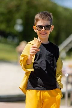Happy little boy eats ice cream in a waffle cone in summer on a walk Stock Photos
