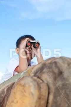 Happy little boy exploring outdoors clambering on a rock with telescope Stock Photos