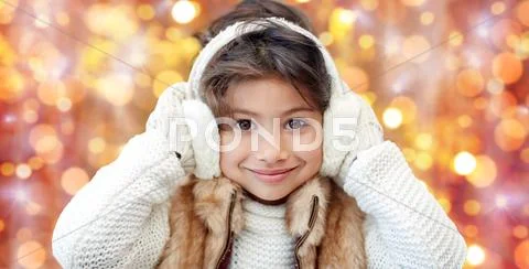 Happy little girl in earmuffs over holidays lights Stock Photos