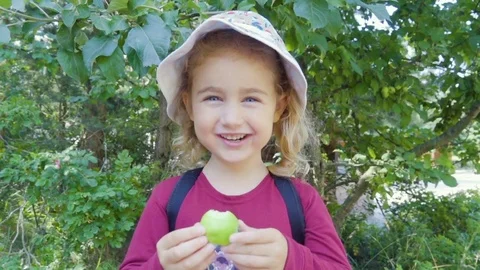 Happy little girl eating sour apple in summer park. Healthy child eats a gree Stock Footage