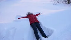 A young woman makes a snow angel lying in the snow with her arms