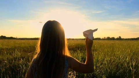 Happy little girl playing with a paper airplane outdoors during sunset Stock Footage