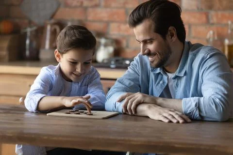 Happy little son and young dad play checkers Stock Photos