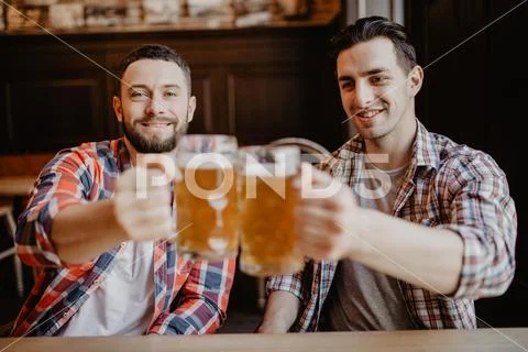 Happy male friends drinking draft beer at bar or pub and clinking glasses Stock Photos