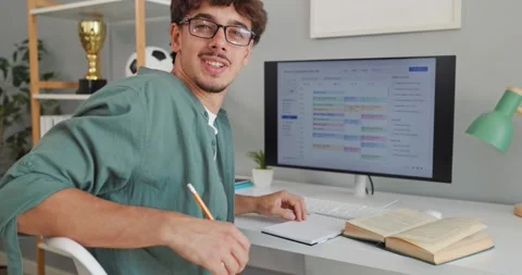 Happy male student studying at computer desk with books at home Stock Footage 345679980