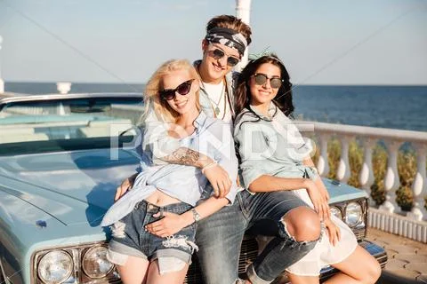Happy man and two women standing together near vintage cabriolet Stock Photos
