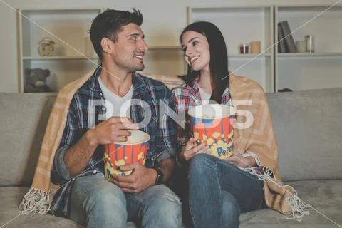 The happy man and a woman eating popcorn and watching movie on the sofa Stock Photos