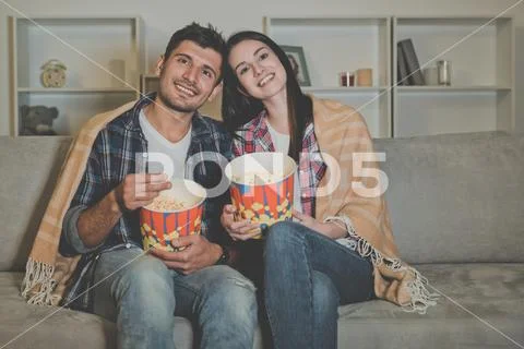 The happy man and a woman eating popcorn and watching movie on the sofa Stock Photos
