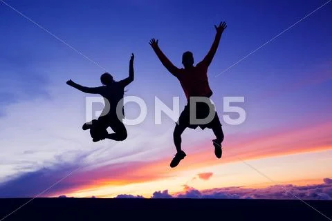 Happy man and woman having fun jumping into air at sunset Stock Photos