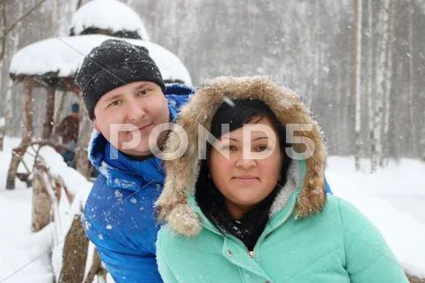 Happy man and woman pose in park during snowfall at winter day Stock Photos