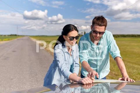 Happy man and woman with road map on car hood Stock Photos