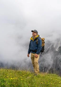 Happy man with backpack standing in Dolomites during rainy weather. Cloud c.. Stock Photos