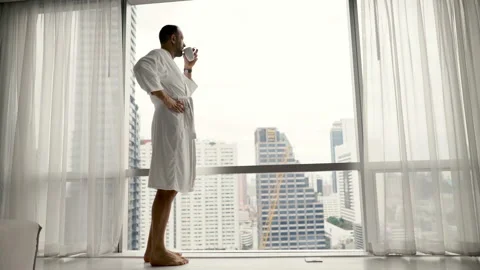 Happy man in bathrobe drinking tea and admire view from window, 4K Stock Footage 127976379