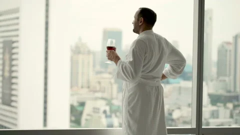 Happy man in bathrobe drinking wine and admire view from window, 4K Stock Footage 127976130