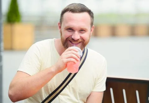 Happy man with a beard drinking a soft drink in the city smiling Stock Photos