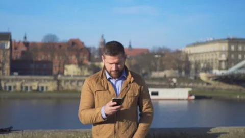 Happy man browsing smartphone walks up and goes away on the background of river Vidéo 72710296