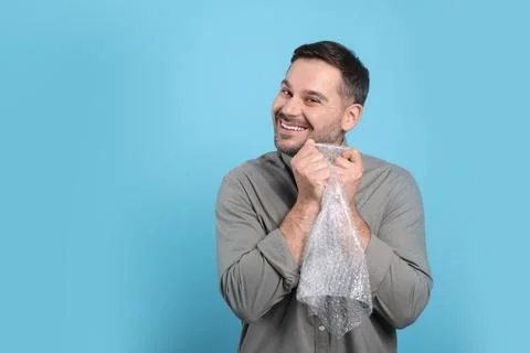 Happy man with bubble wrap on light blue background. Space for text Stock Photos
