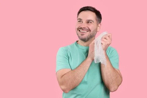 Happy man with bubble wrap on pink background. Space for text Stock Photos
