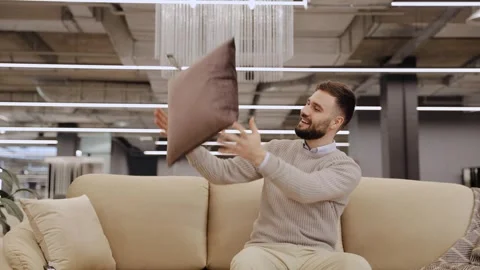 Happy man choosing pillows for sofa in home decor store Stock Footage 322550156