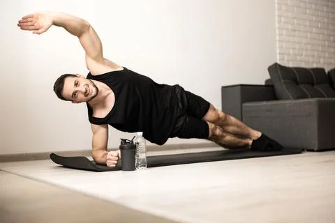 Happy man doing side plank exercise with raised hand, smiling and looking at Stock Photos