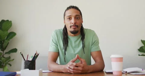 Happy man with dreadlocks sitting at desk, smiling and waving during video call Stock Footage 335925912