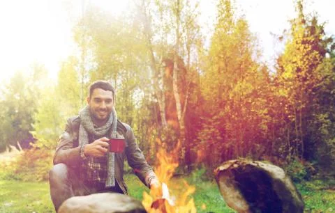 Happy man drinking hot tea near camp fire Stock Photos