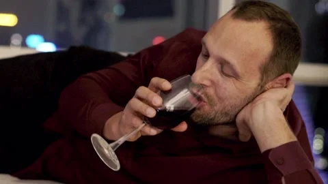 Happy man drinking wine while lying on sofa at home during night 스톡 동영상 98710310