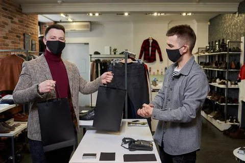 A happy man in a face mask is posing with his purchase in a clothing store. Stock Photos