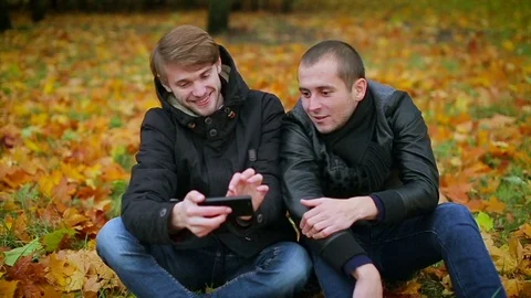 Happy man friends smiling using smartphone in autumn park, dolly shot Stock Footage 73907602