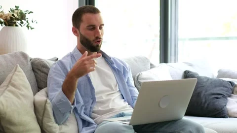 Happy man having a video call on a laptop while sitting on a couch Stock Footage 335588571