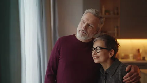 Happy man in his 50s hugging his wife near window, showing love and support Stock Footage 340920233
