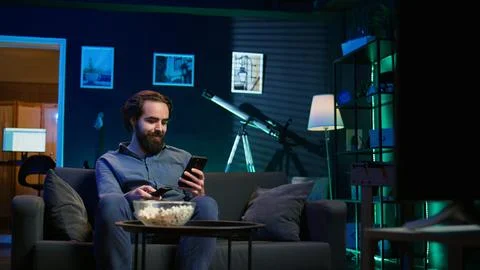 Happy man holding remote control chatting on smartphone Stock Photos