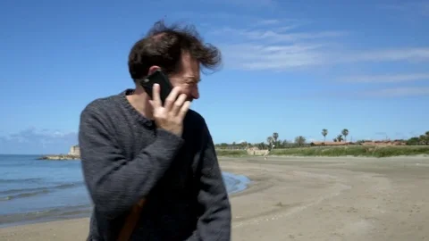 Happy man laughing talking on the phone walking on beach medium shot Stock Footage 75685151