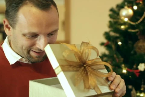 Happy man looking at great gift in the box, christmas tree in background Stock Footage 10741946