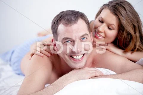Happy man lying in bed with his wife, looking at camera and smiling Stock Photos