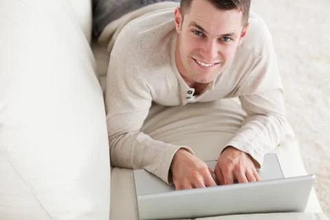 Happy man lying on a couch with a notebook Stock Photos