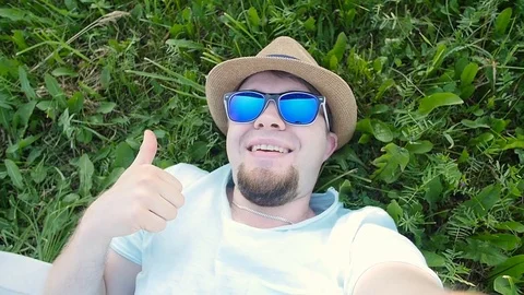 Happy man is lying on a grass in a park taking selfie Stock Footage