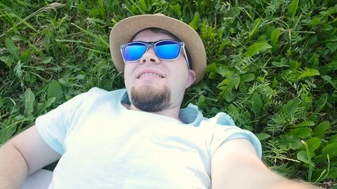 Happy man is lying on a grass in a park taking selfie Stock Footage