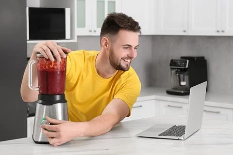 Happy man making smoothie while watching cooking online course in kitchen. .. 스톡 사진