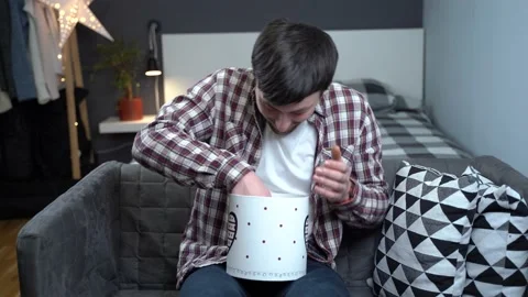 Happy man opens gift box and gets out cute gray kitten at home on couch 스톡 동영상 236935595