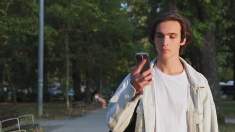 Happy  man in the park communicates using a mobile phone.  Young man is tal.. Stock Footage 254657374
