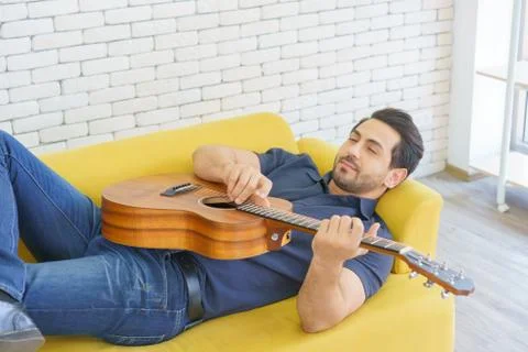 Happy man playing guitar while sitting on sofa in living room, Enjoying caref Stock Photos