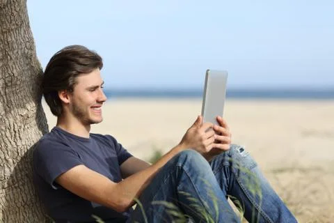 Happy man reading a tablet reader sitting on the beach Stock Photos