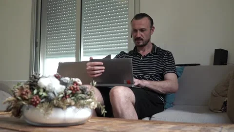 Happy man relaxing on couch while video calling using laptop at home 스톡 동영상 130790323