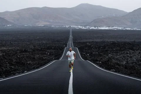 Happy man runner on an empty road through volcanic landscape dusk in Lanzarote Stock Photos