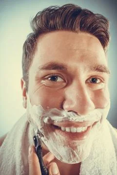 Happy man shaving using razor with cream foam. Photos